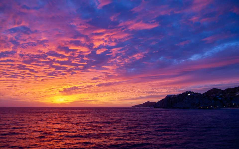 Sunset sky and Land's End bathed in color on a Cabo Rey dinner cruise